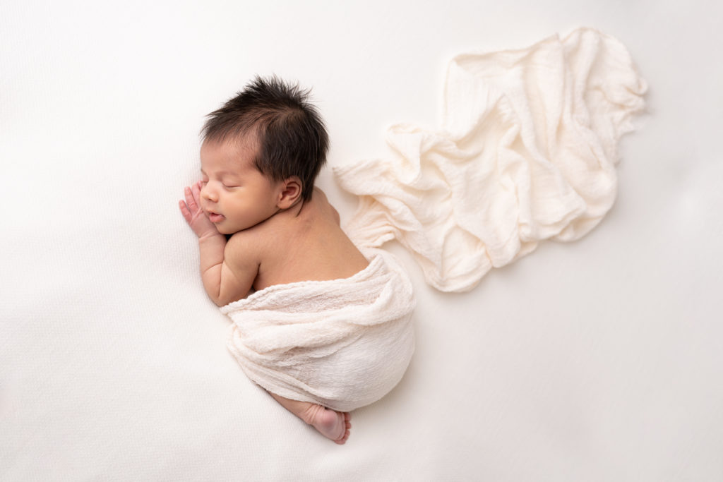 Newborn baby with dark hair asleep lying on a white blanket photographed by Newborn Photographer in Lichfield staffordshire