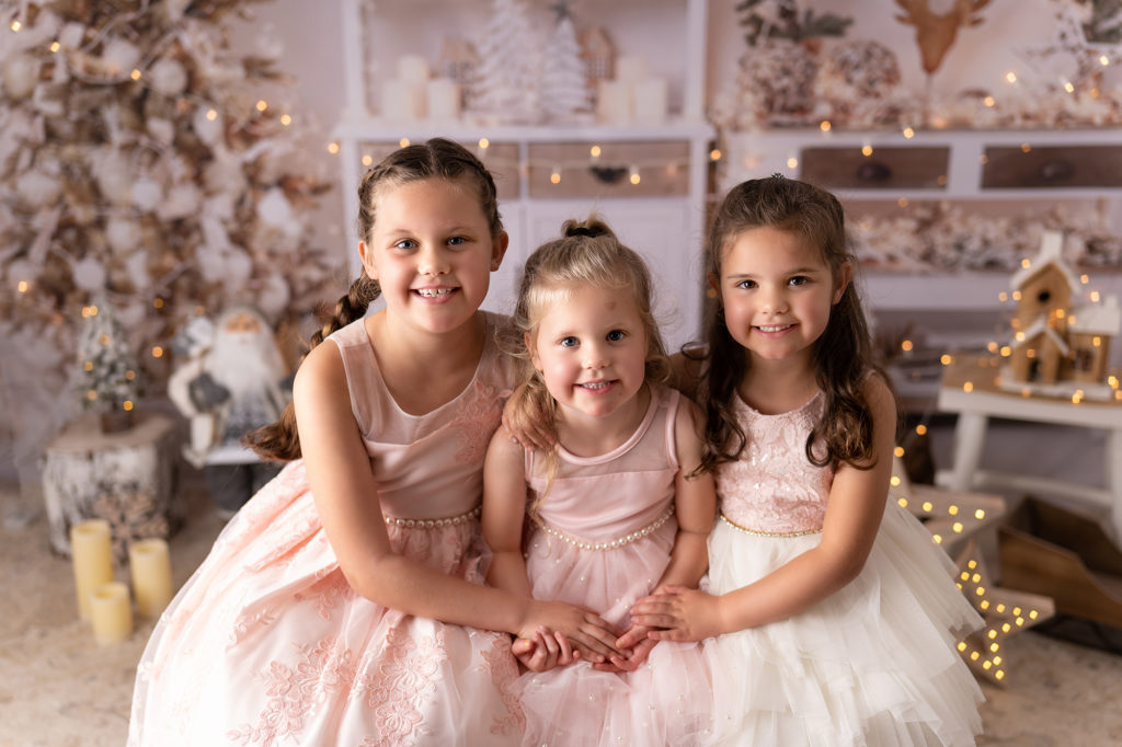 three sisters in white dresses on a festive white background photographed by Newborn Photographer in Lichfield staffordshire